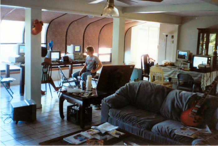 A photo taken by Tom Hall in September 1990, at the lake house in Shreveport, LA, id Software's first office/bachelor pad. In the background, John Carmack (right) and John Romero work on the Super Mario Bros. 3 demo for Nintendo. Sitting in between their computers is an NES running Super Mario Bros. 3, which the "two Johns" played frequently to make sure they nailed the feel of the game. To the right, a desk holds Hall's equipment: a 386/33MHz PC running DOS, and an NES running Super Mario Bros. 3. To capture the exact look and feel of the NES classic, Hall paused the game and duplicated the artwork pixel by pixel. Photo credit: John Romero.